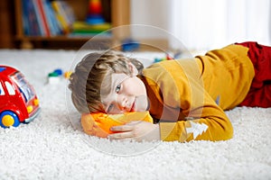 Close-up portrait of little blond kid boy playing at home with toys. Happy smiling child in casual clothes