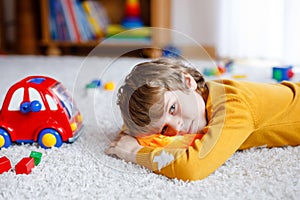 Close-up portrait of little blond kid boy playing at home with toys. Happy smiling child in casual clothes