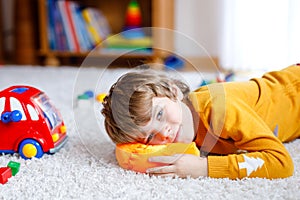 Close-up portrait of little blond kid boy playing at home with toys. Happy smiling child in casual clothes