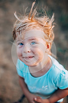 Close up portrait of little blonde girl with blue eyes outside with tousled hair and smiling dirty face. Childhood in the country