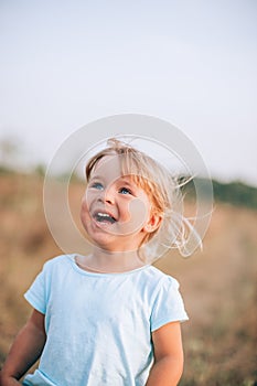 Close up portrait of little blonde girl with blue eyes outside with tousled hair and smiling face. Childhood in the country