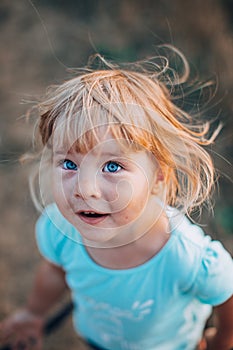 Close up portrait of little blonde girl with blue eyes outside with tousled hair and surprised dirty face. Childhood in the