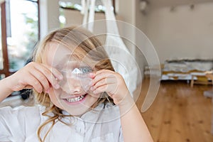 Close-up portrait of little blonde girl holding bright crystal magnifying glass to eye