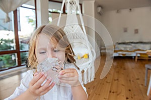 Close-up portrait of little blonde girl holding bright crystal magnifying glass to eye