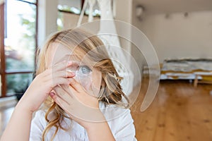 Close-up portrait of little blonde girl holding bright crystal magnifying glass to eye