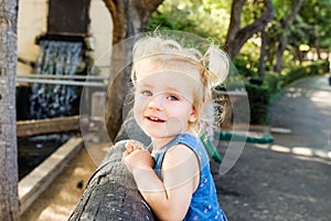 Close up Portrait of little blondy toddler Girl Smiling at Camera. Happy kid walking outdoors in the park or zoo. Family recreatio