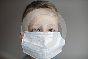Close-up portrait little boy in health mask, looking at the camera on grey background. Virus protection