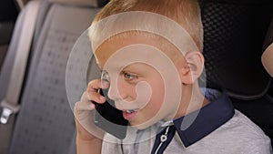 Close-up portrait of a little boy talking on the phone in a car in the back seat