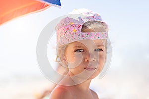 Close up portrait little Caucasian girl on beach skeptical about looking at camera