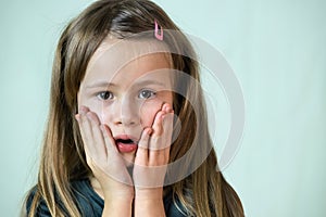 Close-up portrait of little child girl with long hair covering her mouth with hands