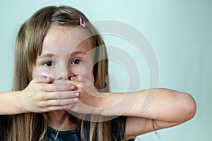 Close-up portrait of little child girl with long hair covering her mouth with hands