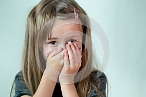 Close-up portrait of little child girl with long hair covering her mouth with hands