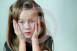 Close-up portrait of little child girl with long hair covering her mouth with hands