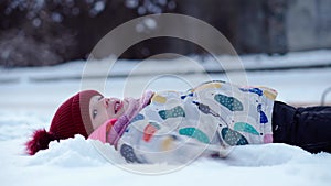 Close up Portrait Little Child Pretty Girl Kid Smiling Looking at Camera play in red hat lie on back. Snow Park Outdoor