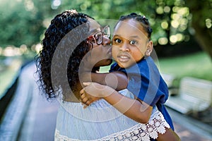 Close up portrait of little cute smiling African child girl in blue dress, looking at camera, while hugging pretty