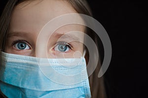 Close-up portrait of little defenseless girl on black backgound in blue disposable mask for protection of Coronavirus