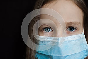 Close-up portrait of little defenseless girl on black backgound in blue disposable mask for protection of Coronavirus