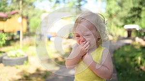 Close up portrait of little funny cute blonde girl child toddler in yellow bodysuit crying outside at summer. Childish