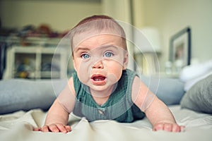 Close up portrait of little funny cute blonde infant boy child toddler with blue eyes in green linen bodysuit crying