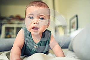 Close up portrait of little funny cute blonde infant boy child toddler with blue eyes in green linen bodysuit crying