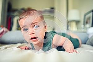 Close up portrait of little funny cute blonde infant boy child toddler with blue eyes in green linen bodysuit crying