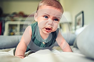 Close up portrait of little funny cute blonde infant boy child toddler with blue eyes in green linen bodysuit crying