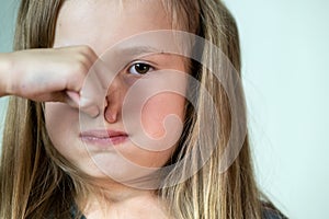 Close-up portrait of little girl with long hair holding her nose with fingers in disgust