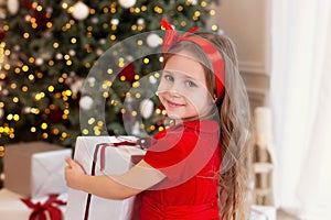 Close-up portrait Little girl in a red dress laughs and enjoys the gift. Little girl opening a magical christmas present at home.