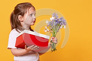 Close up portrait of little girl with red gift box and bouquet of blue florets, preparing to congratulate her mommy with Mother`s