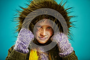 Close up portrait of little girl in warm autumn jacket with fur hood in green and mittens, shot on blue