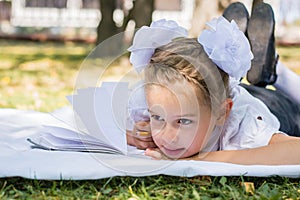 Close-up portrait of a little schoolgirl doing homework while lying on a blanket in a sunny autumn park. Outdoor education for