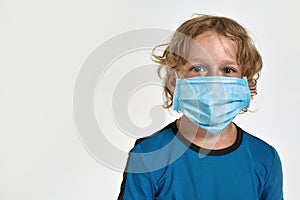 Close up portrait of little sportive boy child in sportswear wearing medical mask, looking at camera while posing
