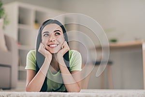 Close-up portrait of lovely cheery creative long-haired girl lying on carpet thinking creating solution at light