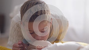 Close-up portrait loving Caucasian teenage brother admiring kissing infant baby sister. Happy smiling boy taking care of