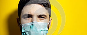 Close-up portrait of male face, wearing medical flu mask on background of yellow color with copy space.