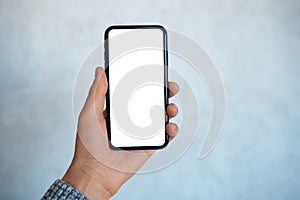 Close-up portrait of male hand, holding a smartphone with mockup, on the background of light grey wall