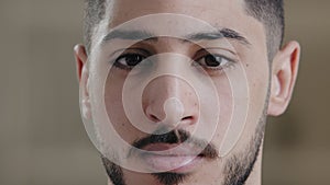 Close-up portrait of male serious young student freelancer arab bearded man stand indoor looking at camera with