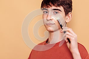 Close-up of a portrait of a male teenager applying cream to his cheek. The boy takes care of the skin of the face. A teenager