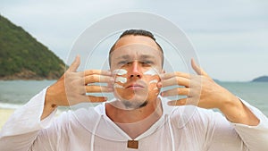 Close-up portrait man apply sun cream protection lotion, looking at camera.Stylish men on beach near sea smearing