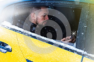 Close-up portrait of a man, a car passenger take on the phone looking out the open window in winter