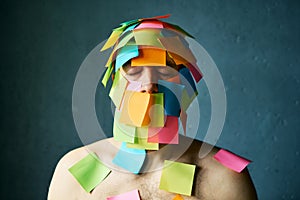 Close up portrait of man with closed eyes and colorful sticky notes all over his face and body over gray background