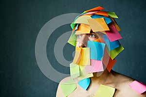 Close up portrait of man covered with colorful sticky notes all over his face and body over gray background