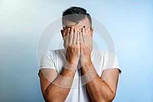 Close-up portrait of a man, covering his face with his hands. On a light background. The concept of body language