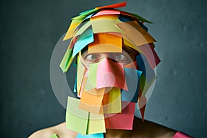 Close up portrait of man with cross-eyed covered with colorful sticky notes all over his face and head