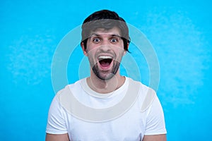 Close up portrait of man, guy is shocked, extremely happy, with wide open eyes and mouth on blue background