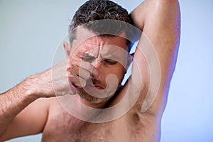 Close up portrait of man, smelling his armpit, feeling bad odor, wants to take a shower, needs antiperspirants