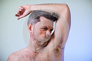 Close up portrait of man, smelling his armpit, feeling bad odor, wants to take a shower, needs antiperspirants