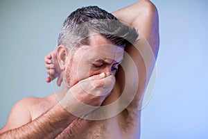 Close up portrait of man, smelling his armpit, feeling bad odor, wants to take a shower, needs antiperspirants