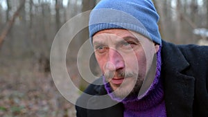 Close-up portrait of a man who smokes and drinks tea from a metal mug in the forest, looks into the camera.