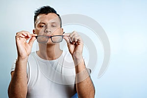 A close-up portrait of a man who straightens his glasses with his hands. On a light background